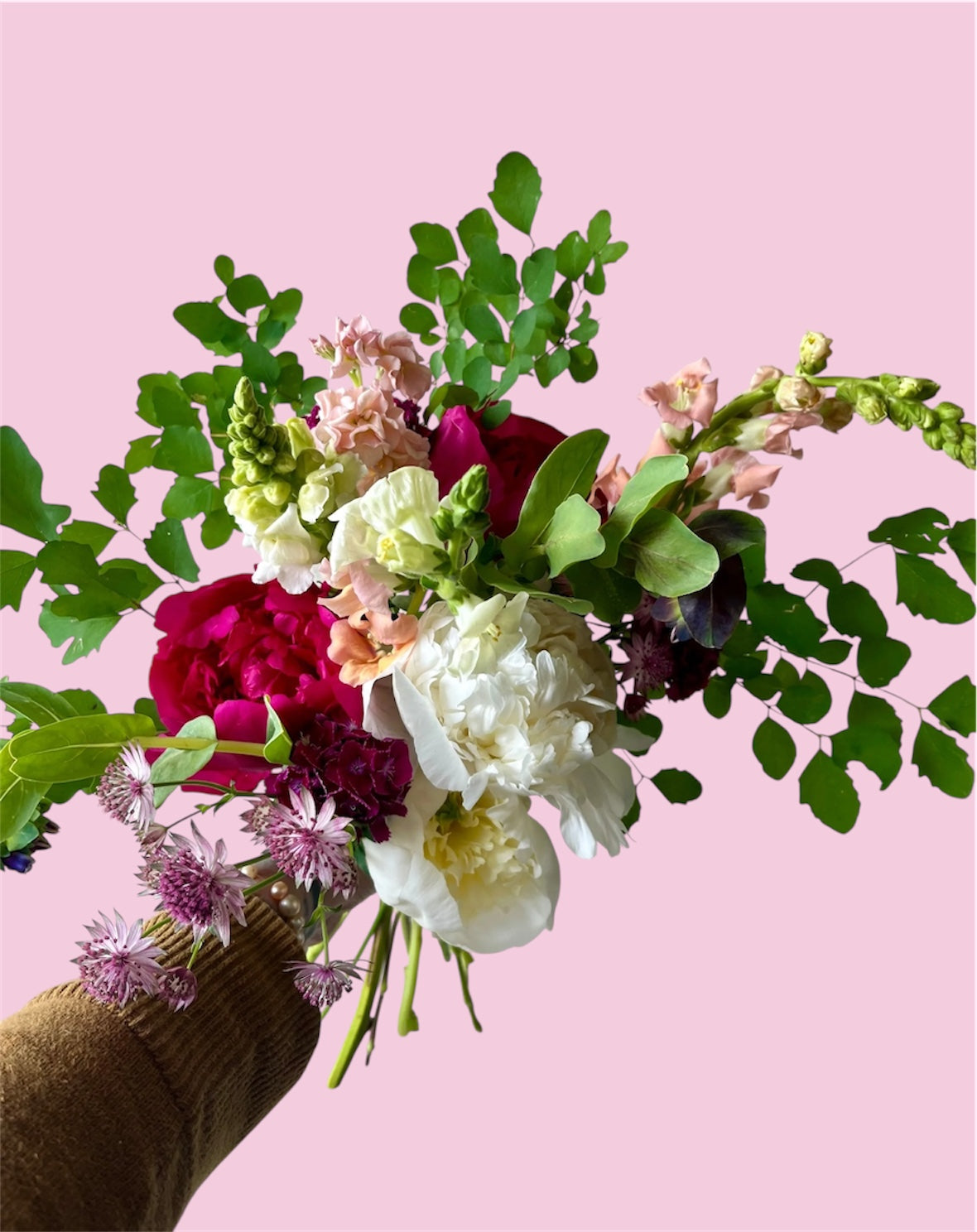 Floral arrangement with green leaves and pink flowers on a pink background