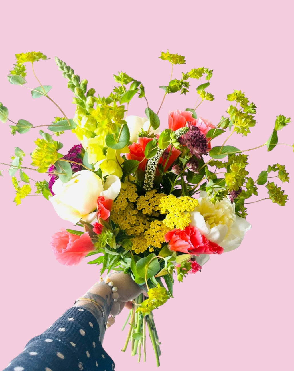 Bouquet of colorful flowers held against a pink background
